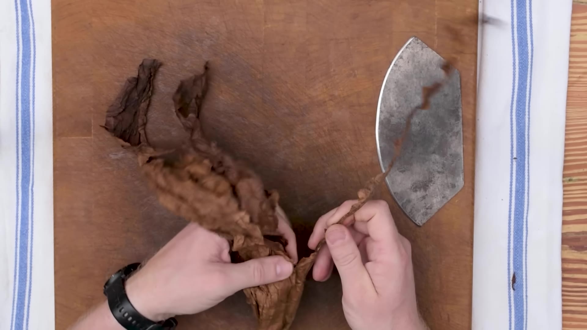 Hands folding tobacco filler leaves together into a bunch on a wooden board
