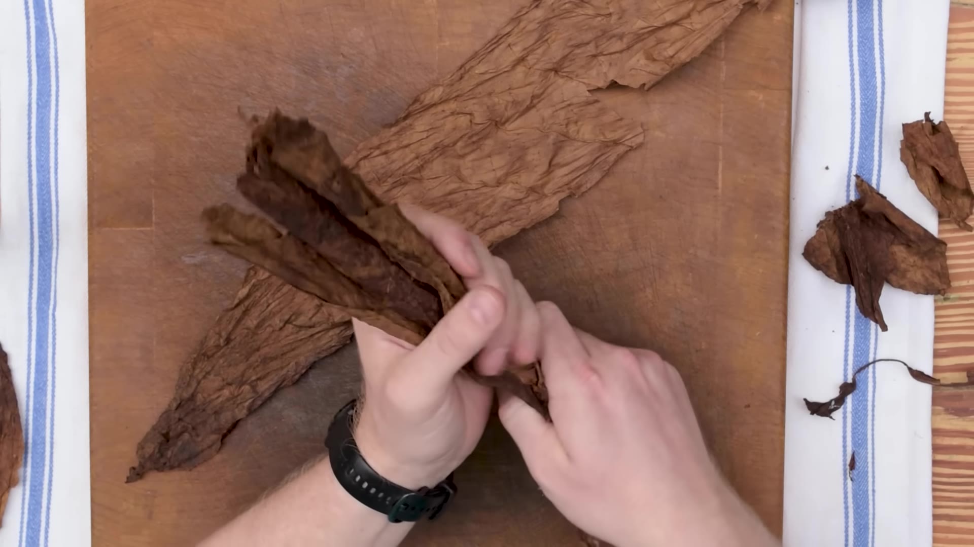 Several long tobacco filler leaves laid out on a wooden board next to a chaveta blade