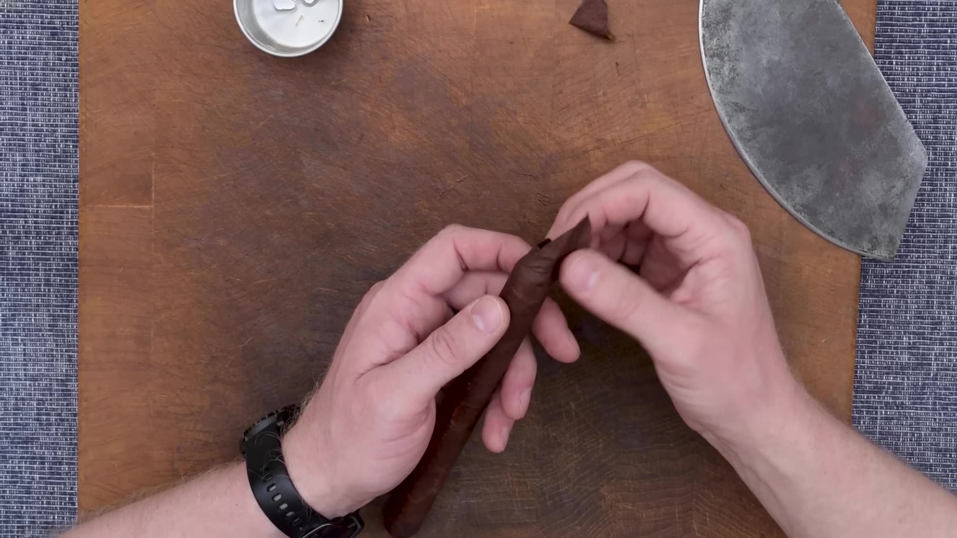 Hands pressing a small round cap of wrapper leaf onto the head of the cigar, glue pot nearby